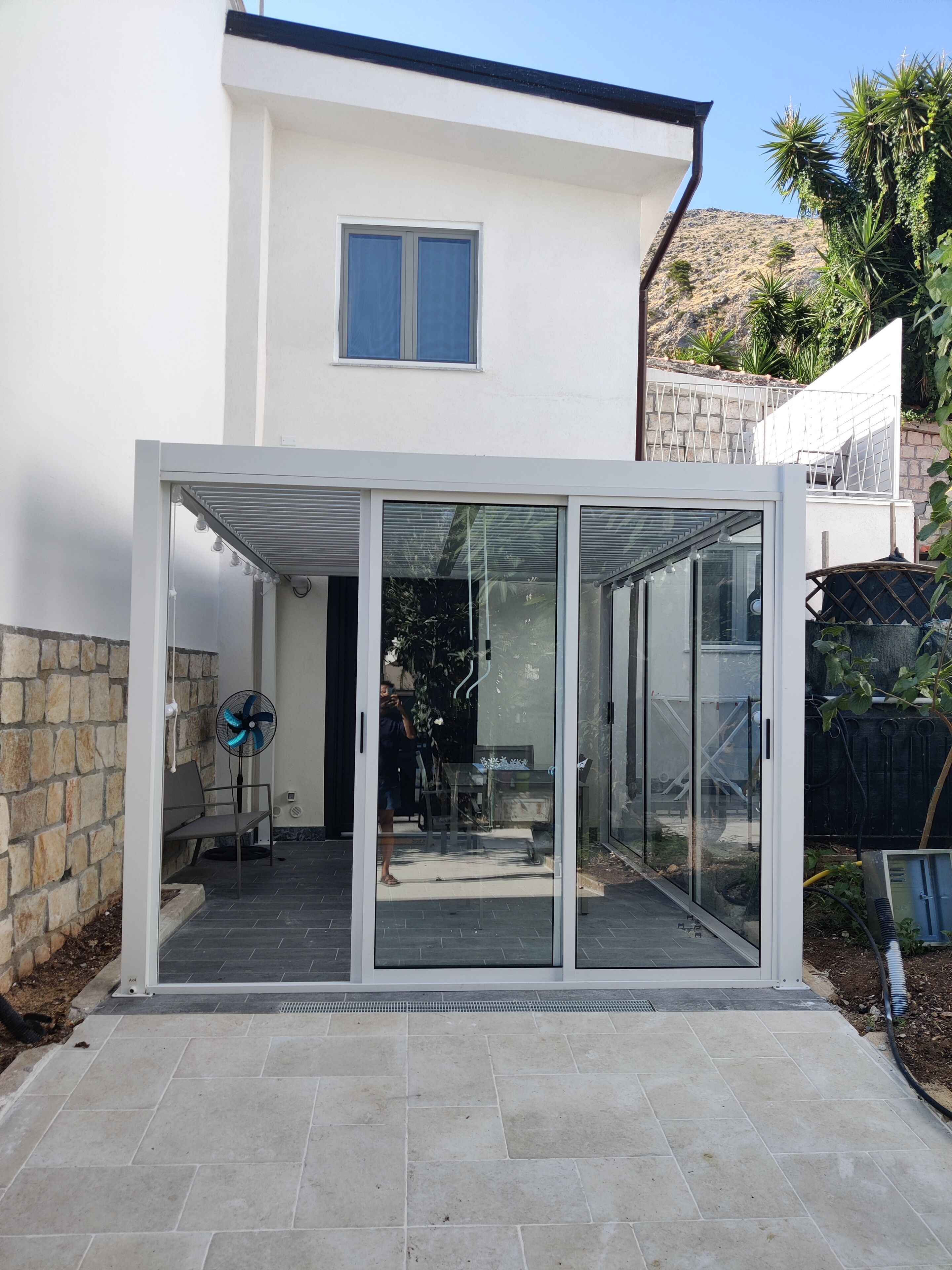 Une maison moderne dotée d’un patio entièrement vitré, d’un mur en pierre et d’une montagne en toile de fond.