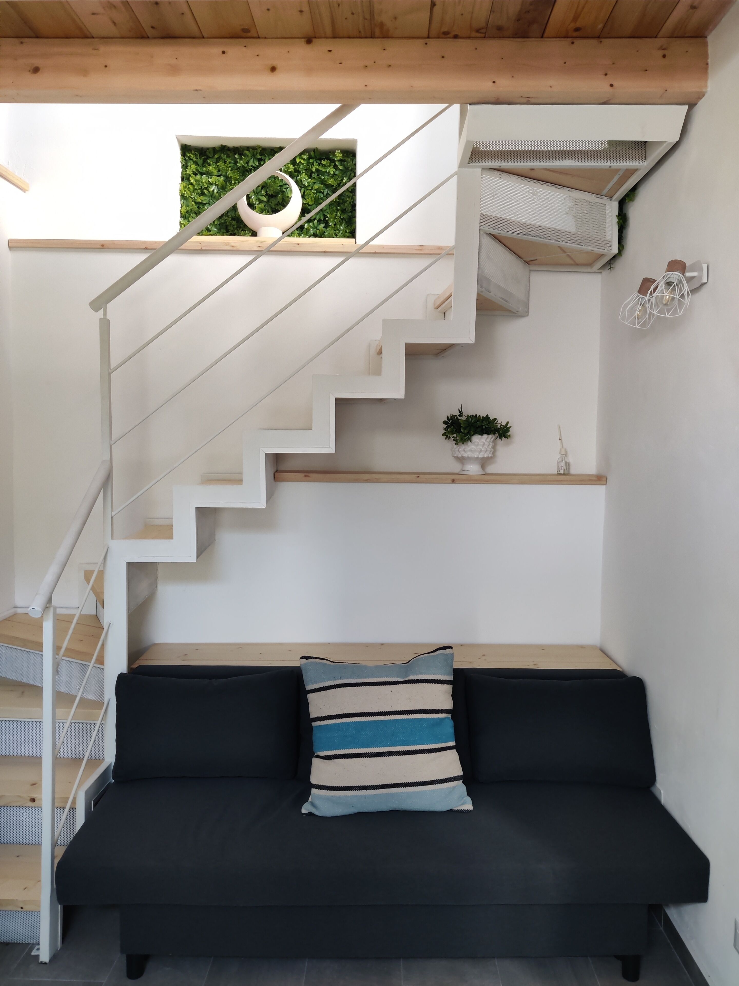 Um interior moderno com uma escada, um sofá preto e uma pequena planta.