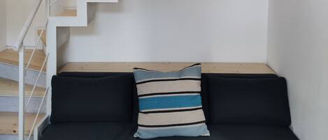 A modern interior with a staircase, a black sofa, and a small plant.