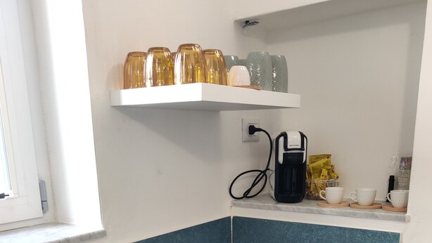 Ett kök med en dubbeldiskho, en kaffebryggare och en hylla ovanför diskhon med burkar.