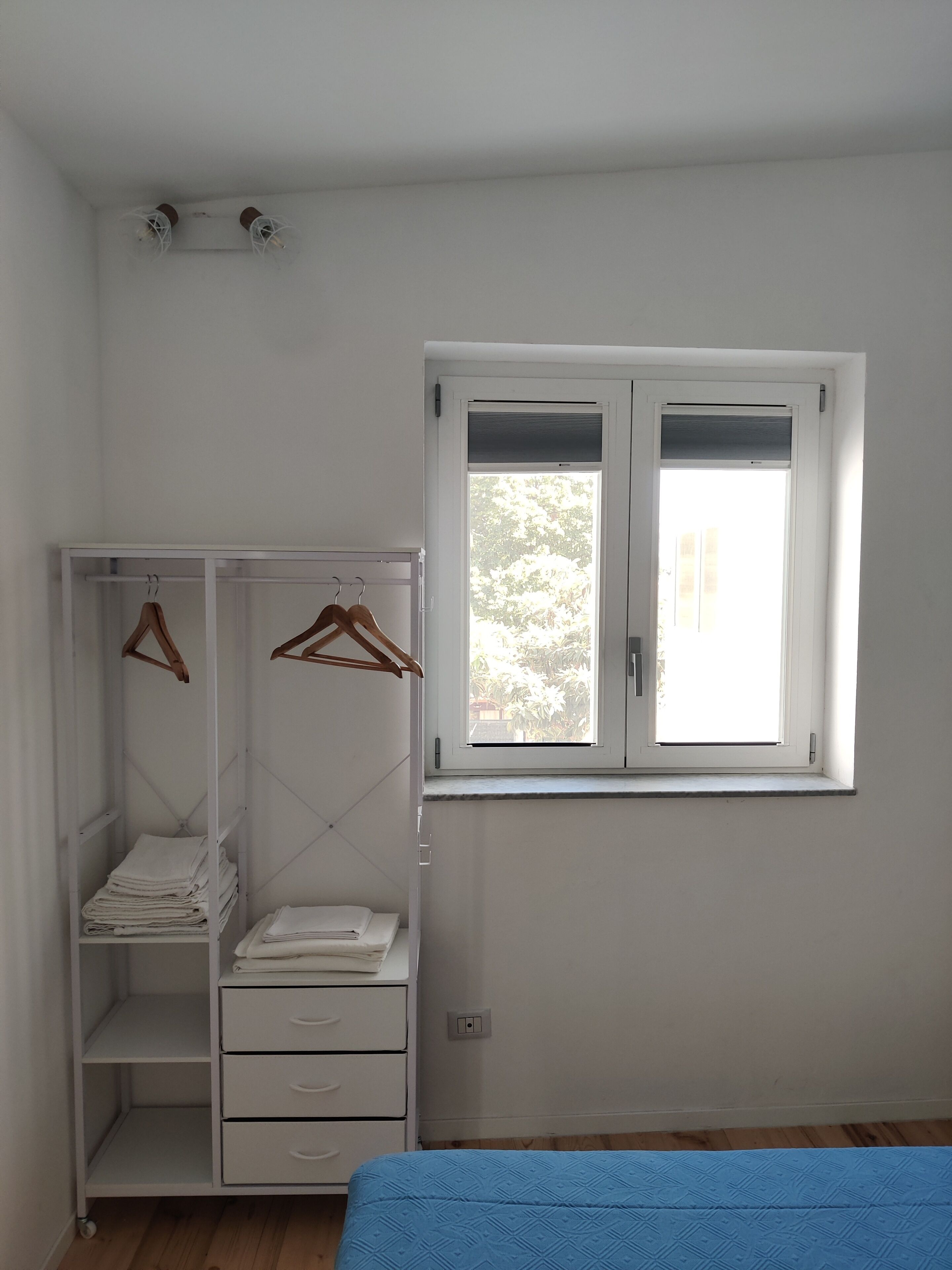Een slaapkamer met een enkel bed, een kledingkast met ophangruimte en een raam met zonwering.