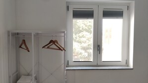 Ett sovrum med en säng, en garderob med plats för att hänga kläder och ett fönster med persienner.