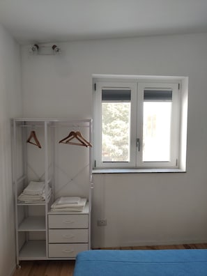 A bedroom with a single bed, a wardrobe with hanging space, and a window with blinds.