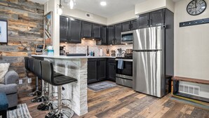 Una cocina moderna con gabinetes oscuros, electrodomésticos de acero inoxidable y una zona de bar con taburetes.