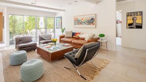A modern living room with a brown leather sofa, a black armchair, and a coffee table. There is a painting on the wall and a small table with a lamp. - Charming 2-bedroom Mid-Century Modern house in enchanting Palm Springs (Palm Springs)