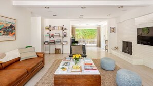 A modern living room with a brown leather sofa, a coffee table with books and flowers, a bookshelf, and a fireplace. - Charming 2-bedroom Mid-Century Modern house in enchanting Palm Springs (Palm Springs)