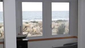 A room with a large window overlooking a rocky shoreline and the sea. There is a desk with a computer and a chair. - Ultimate OceanFront 2BRs Penthouse & private beach (Sea Bright)