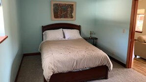 Un dormitorio con una cama individual, una mesita de noche, un cuadro en la pared y una puerta que da a otra habitación.