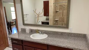 Un baño con encimera de granito, lavamanos blanco y un espejo grande.
