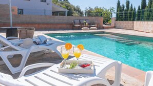 A poolside area with lounge chairs, a tray with drinks and fruit, and a view of the pool. - El Real de Magiaza Riogordo by Ruralidays (Málaga)