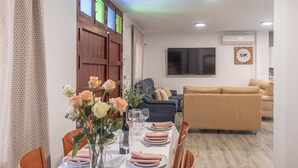 A dining area with a table set for four, a sofa, and a TV in the background. - El Real de Magiaza Riogordo by Ruralidays (Málaga)