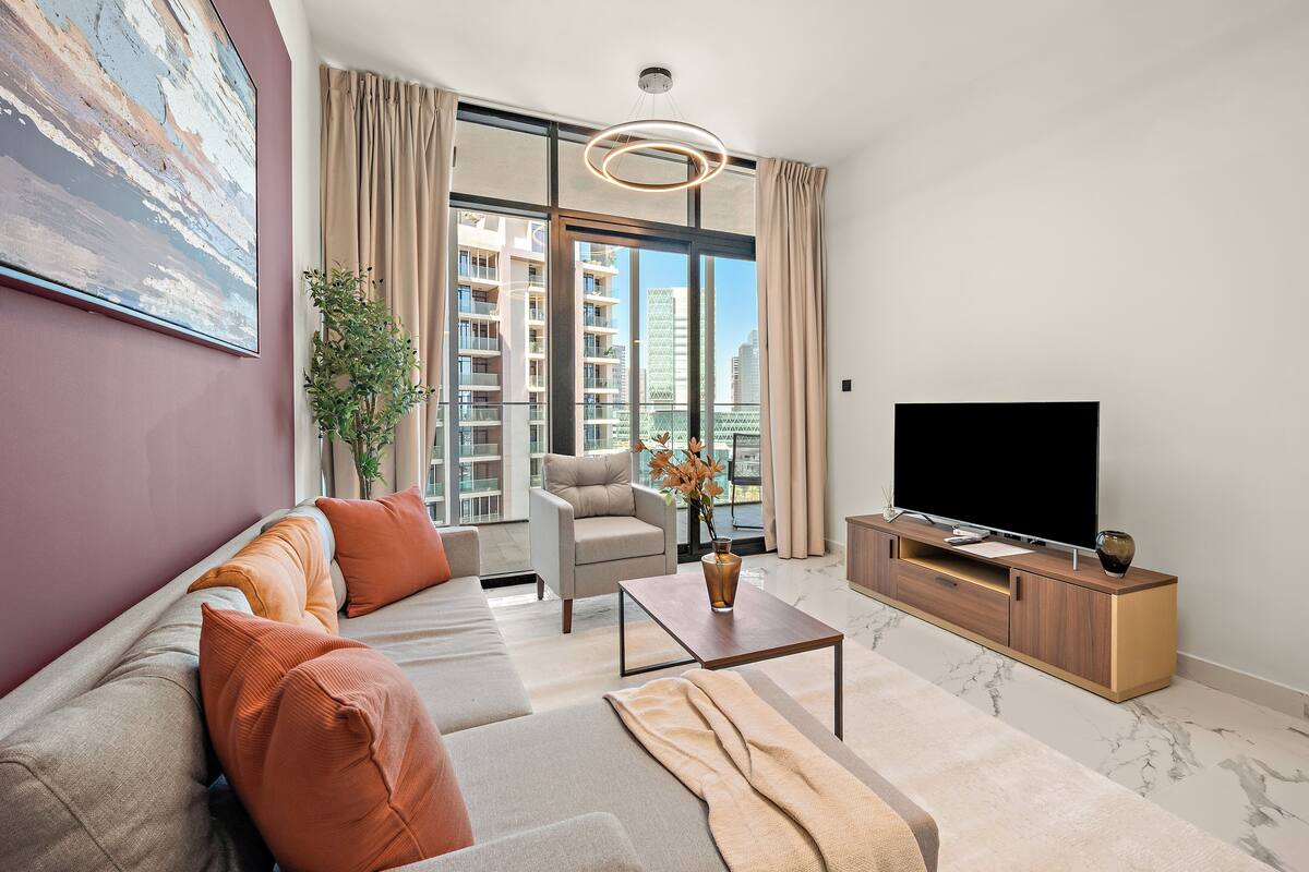 A modern living room with a sofa, armchair, coffee table, TV, and a large window with a city view.