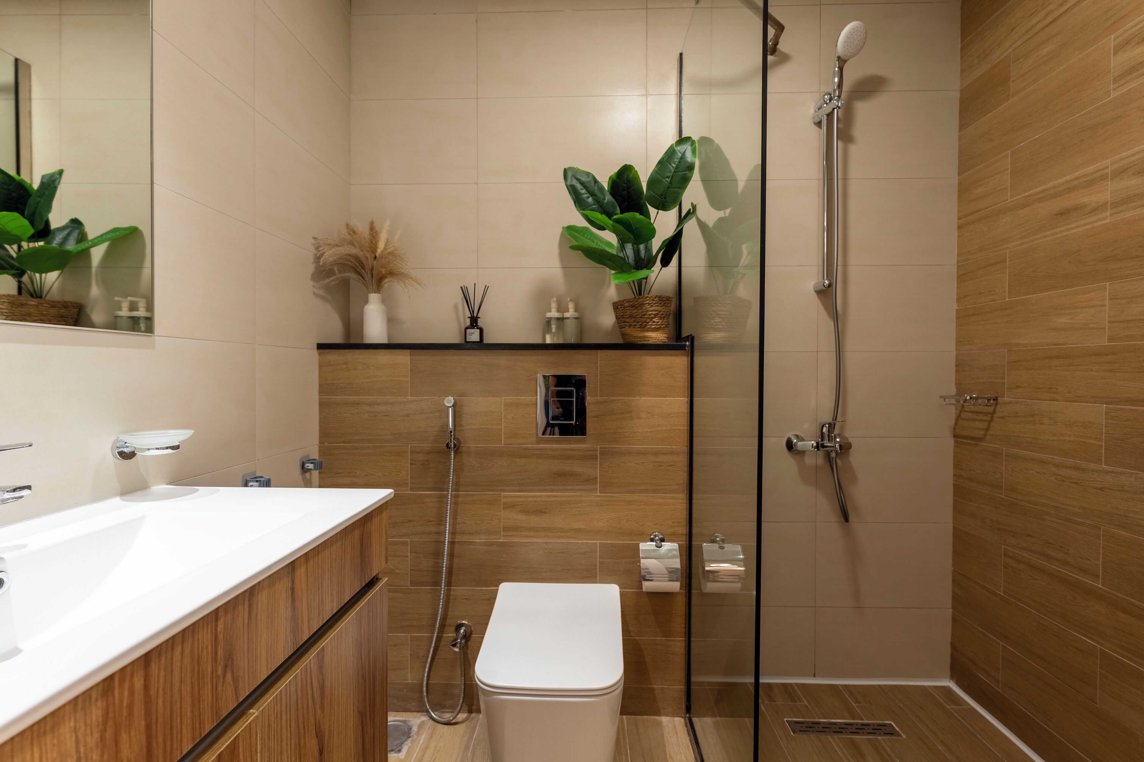 Un baño moderno con tocador de madera, cabina de ducha de vidrio y plantas en macetas.