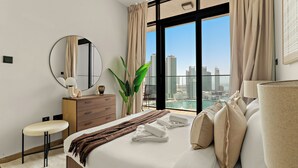 A modern hotel room with a large bed, a round mirror, a nightstand, a desk, and a view of the cityscape. - Silkhaus Al Maryah Vista 1 (Abu Dhabi)