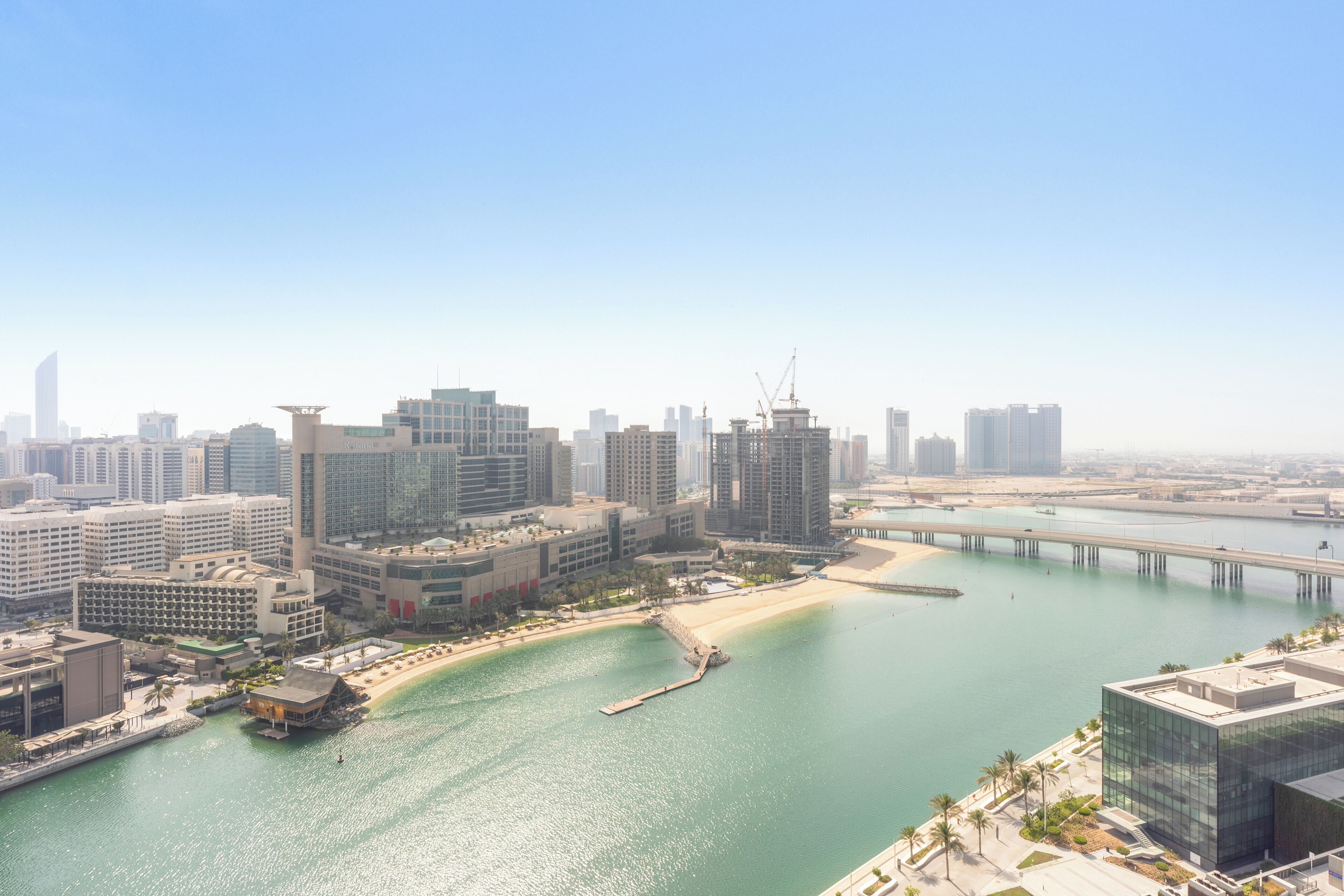 A coastal cityscape with modern high-rise buildings, a marina, and a bridge.