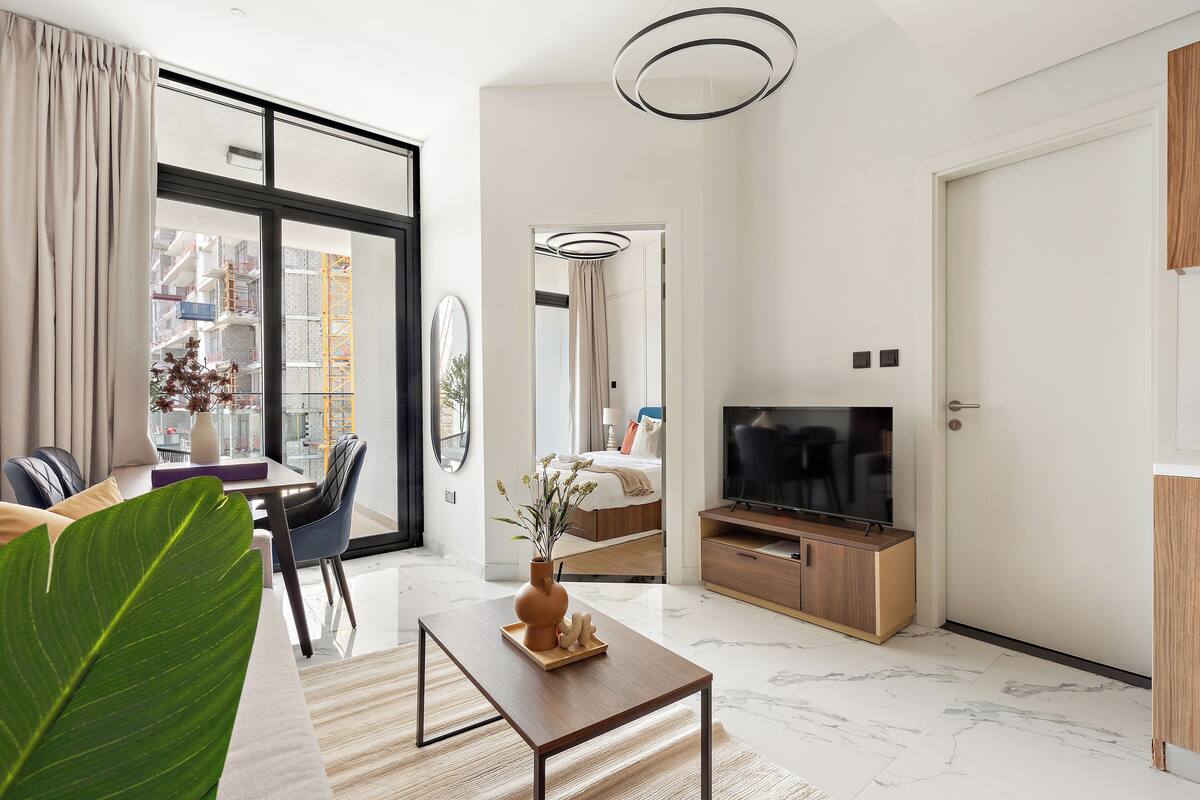 A modern living room with a large window, a dining area, a TV, and a wooden cabinet.