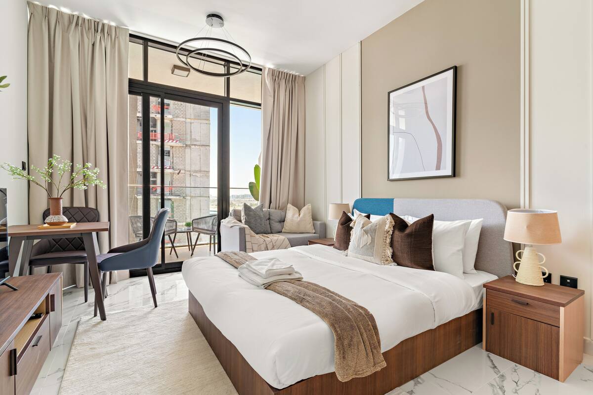 A hotel room with a large bed, a desk, a chair, and a balcony with curtains.