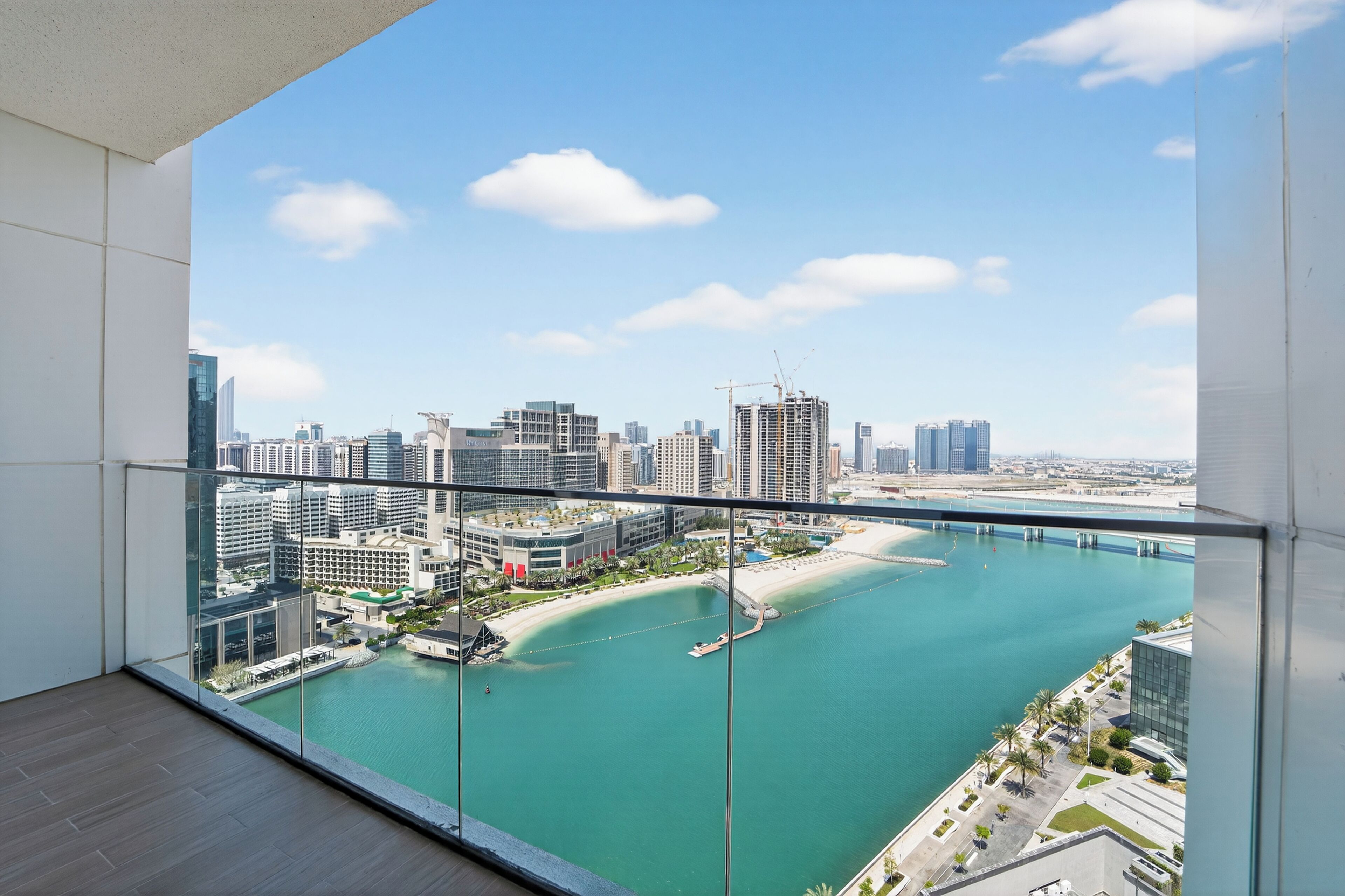 Un immeuble de grande hauteur doté d’un balcon en verre offrant une vue sur un port de plaisance et le paysage urbain.