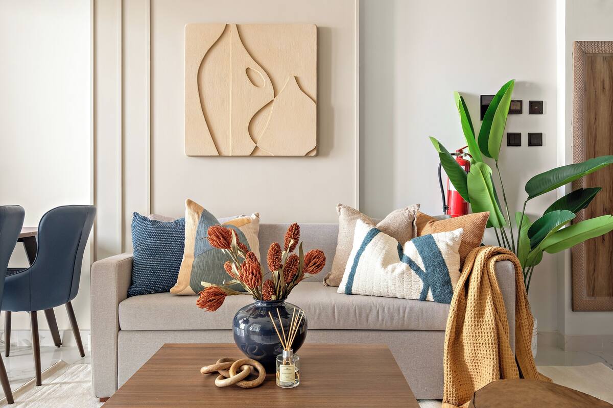 A modern living room with a sofa, decorative pillows, a vase with dried flowers, a wooden coffee table, and a large green plant.