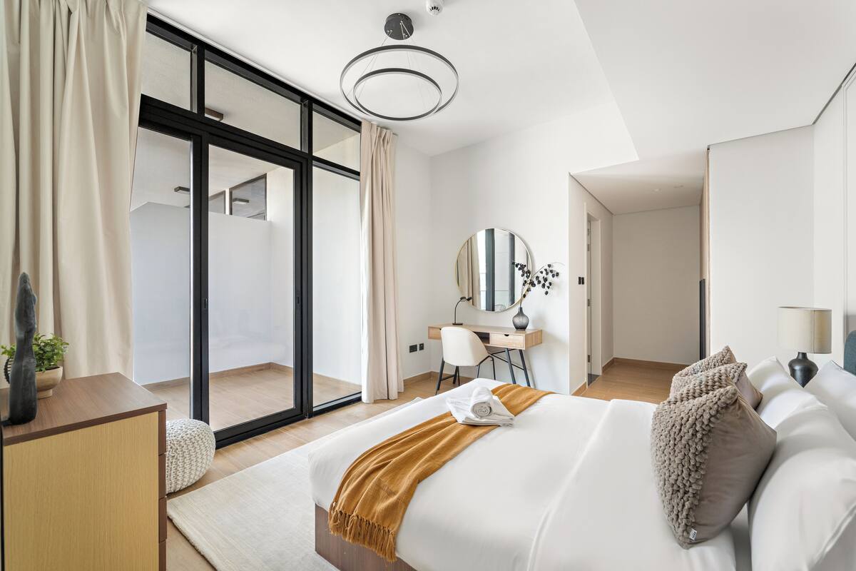 A modern hotel room with a large bed, a desk, and a sliding glass door leading to a balcony.