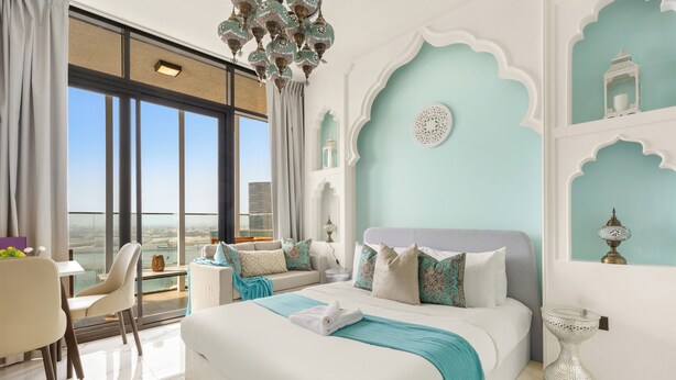 A modern bedroom with a large bed, a view of the city, and a balcony with a dining area. - Silkhaus Al Maryah Vista 1 (Abu Dhabi)