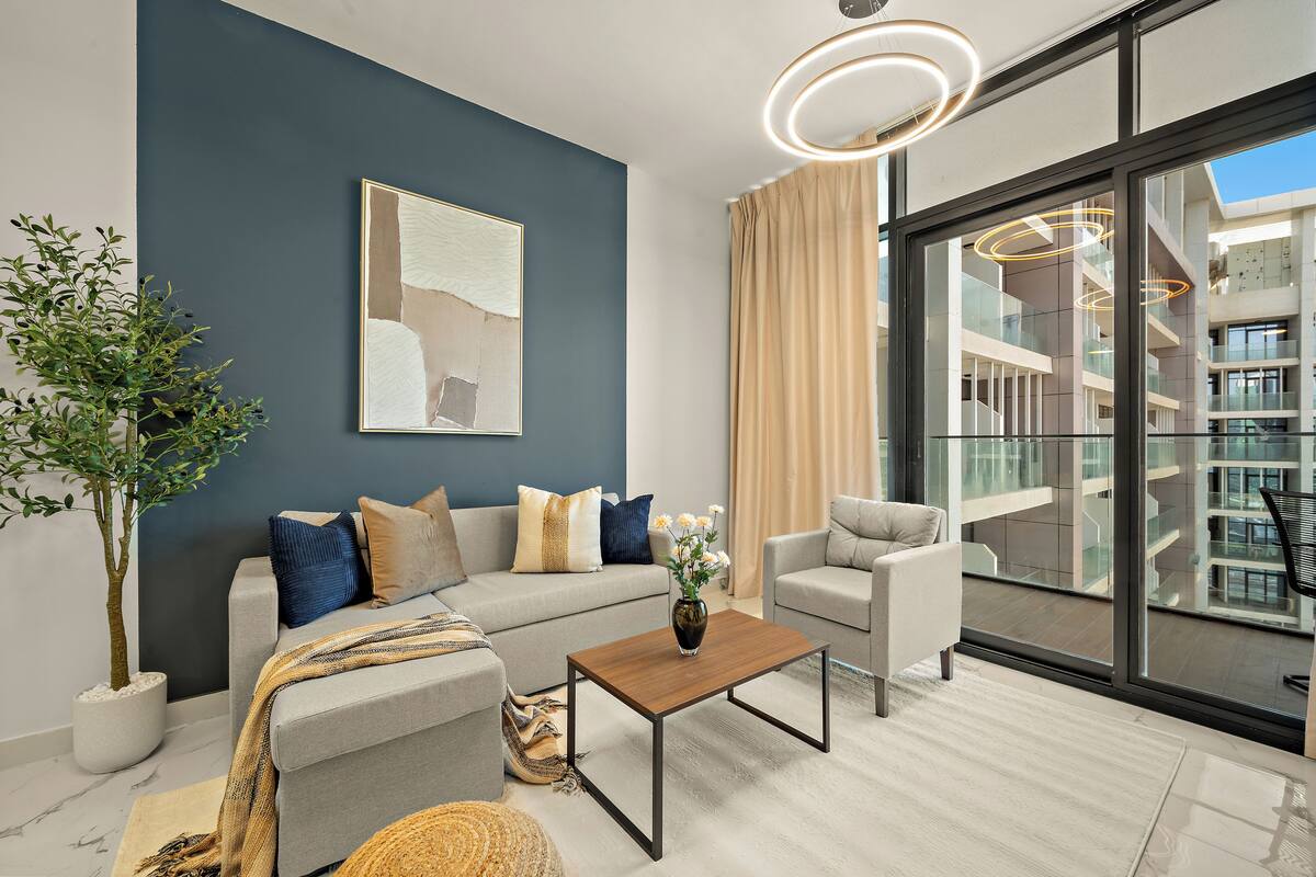 A modern living room with a grey sofa, a wooden coffee table, and a large window offering a view of a building's interior.
