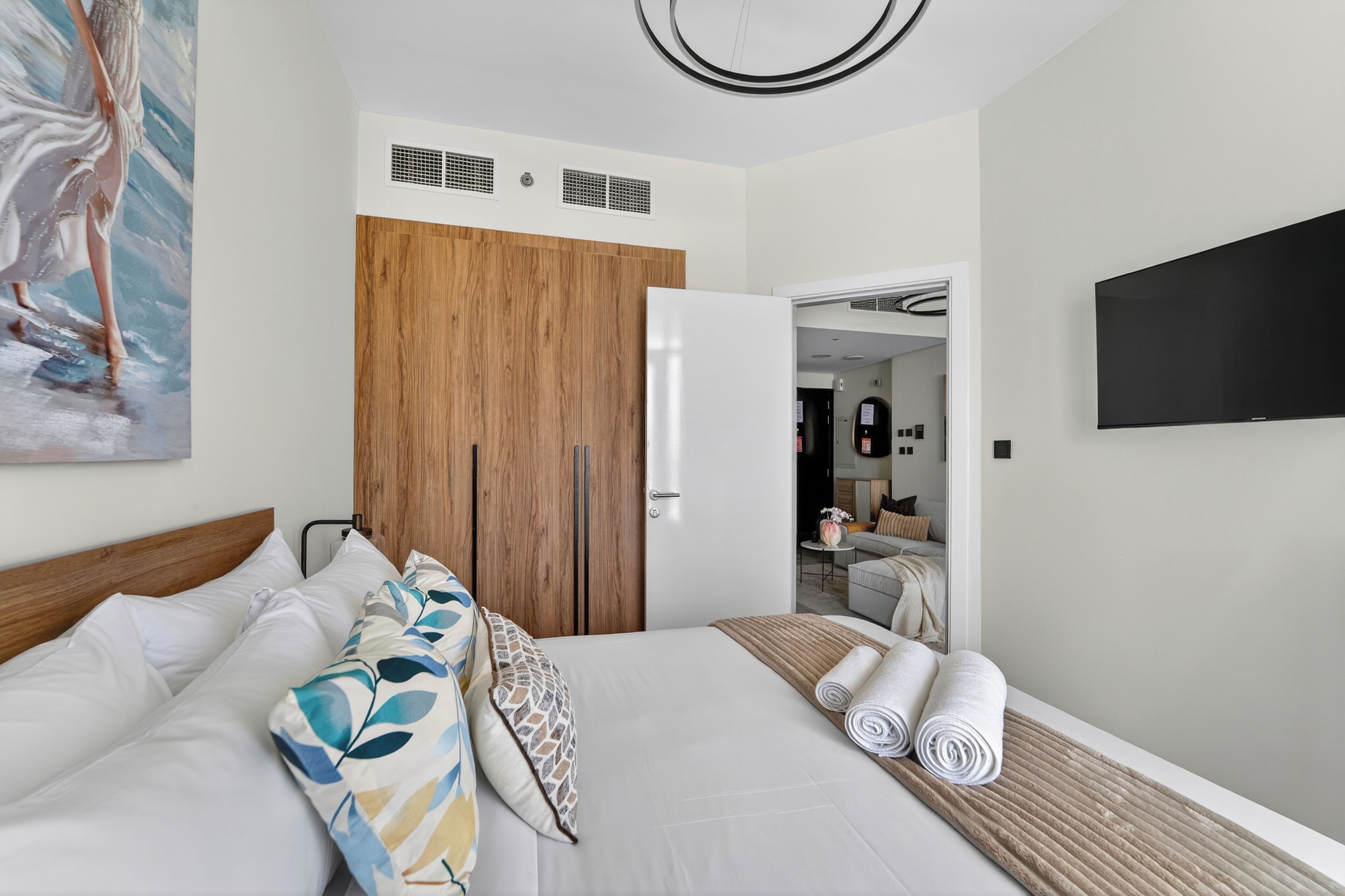 Habitación de hotel con cama, armario de madera, televisión y baño a la vista a través de una puerta abierta.