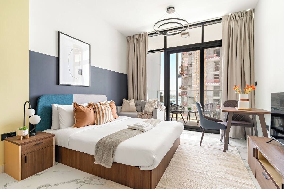 A modern hotel room with a large bed, a desk, a chair, and a TV.