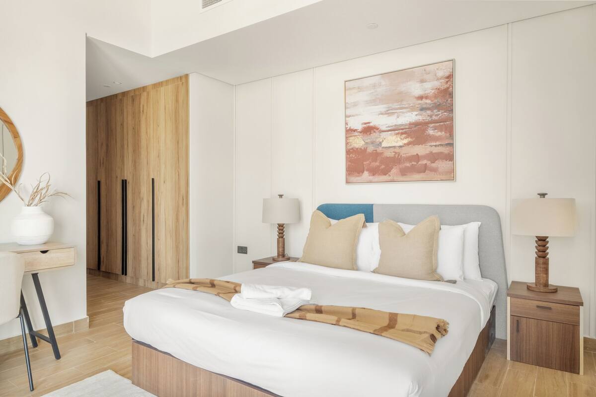 A modern hotel room with a large bed, wooden wardrobe, and a painting on the wall.