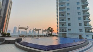 A swimming pool area with a sunken design, surrounded by a modern building with balconies. - Silkhaus Amaya Towers (Abu Dhabi)