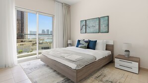 A modern bedroom with a large bed, a nightstand, and a view of the city through floor-to-ceiling windows. - Silkhaus Amaya Towers (Abu Dhabi)