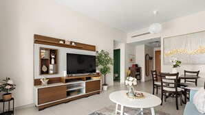 A modern living room with a flat-screen TV, wooden entertainment unit, dining table, and chairs. - Silkhaus Amaya Towers (Abu Dhabi)