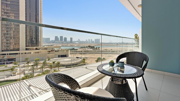 A balcony with a glass table and chairs, overlooking a cityscape with tall buildings and a beach. - Silkhaus Amaya Towers (Abu Dhabi)