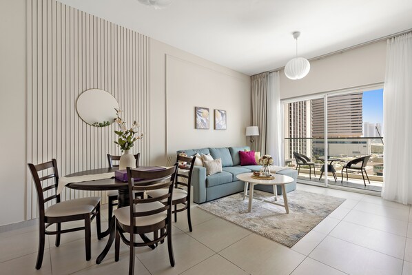 A modern living room with a dining area, a sofa with cushions, a round table, and a balcony with chairs.