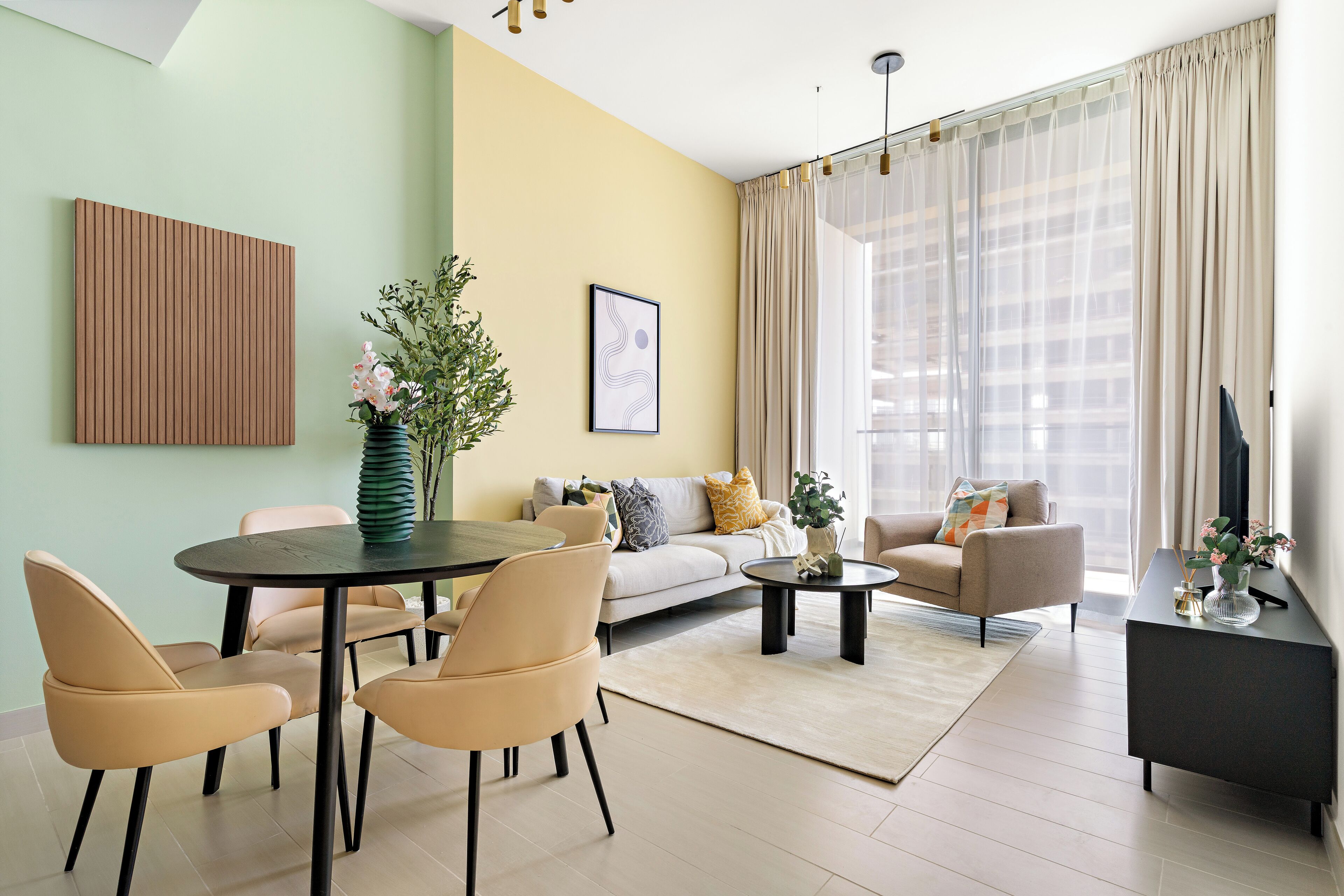 A modern living room with a round dining table, beige chairs, a sofa, and a TV on a black stand.