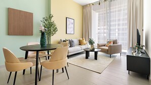 A modern living room with a round dining table, beige chairs, a sofa, and a TV on a black stand.
