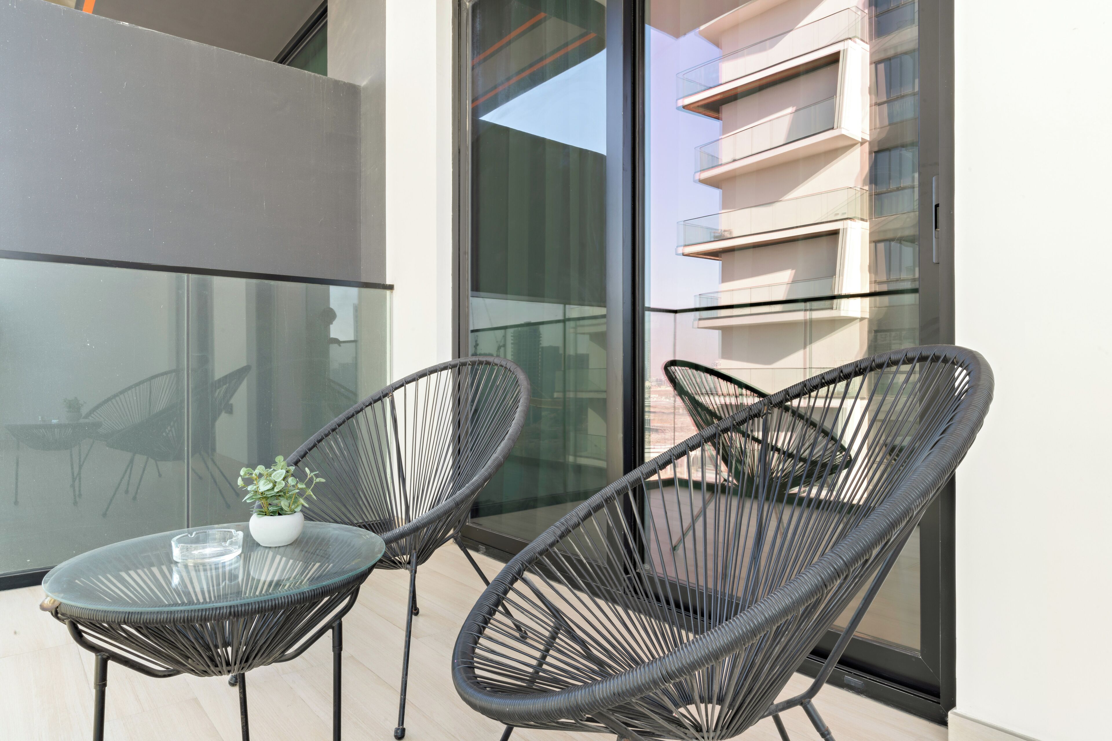 A balcony with two wicker chairs and a small table with a plant and ashtray.