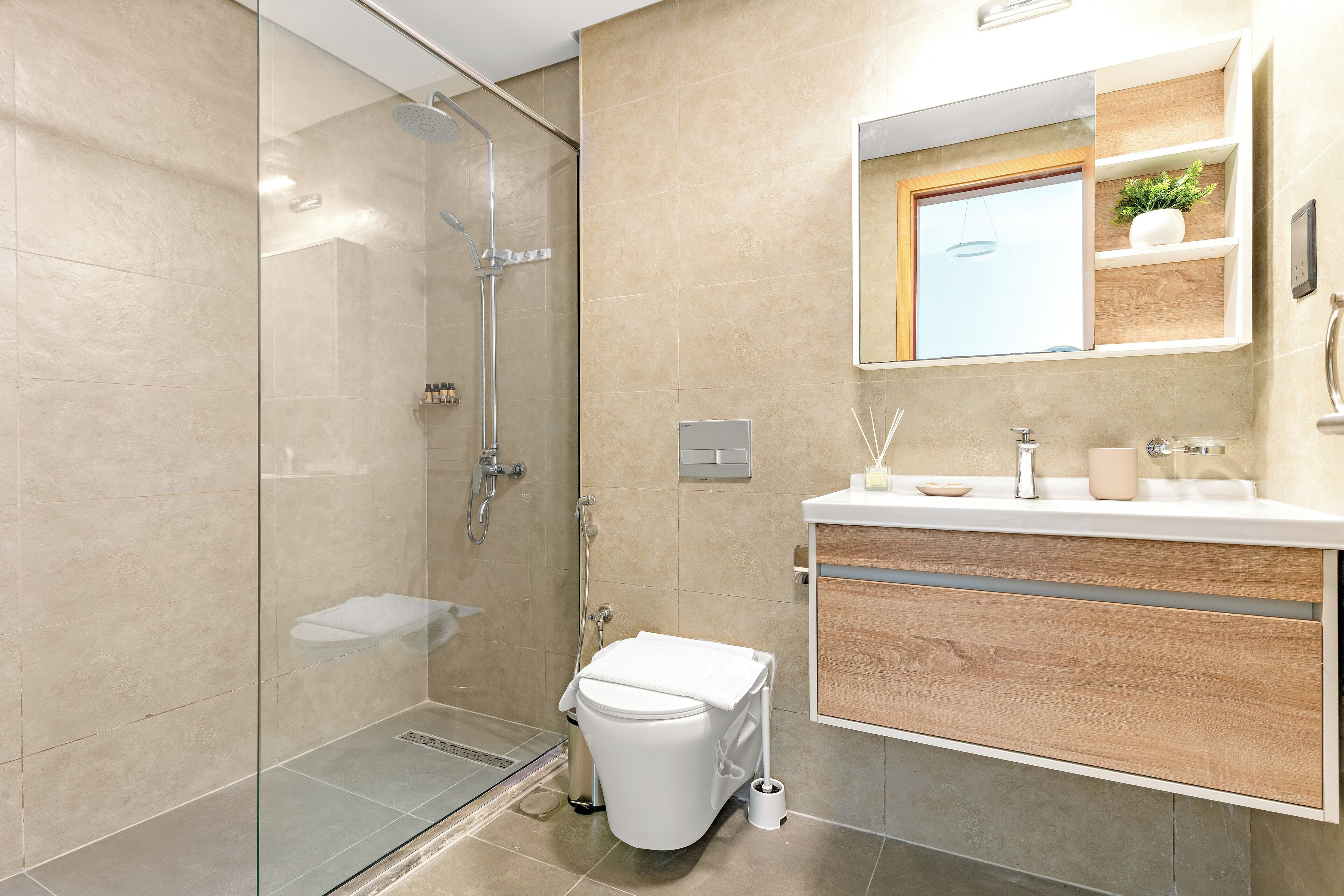 Een moderne badkamer met een douche met glazen wand, een toilet en een wastafel met spiegel en planken.