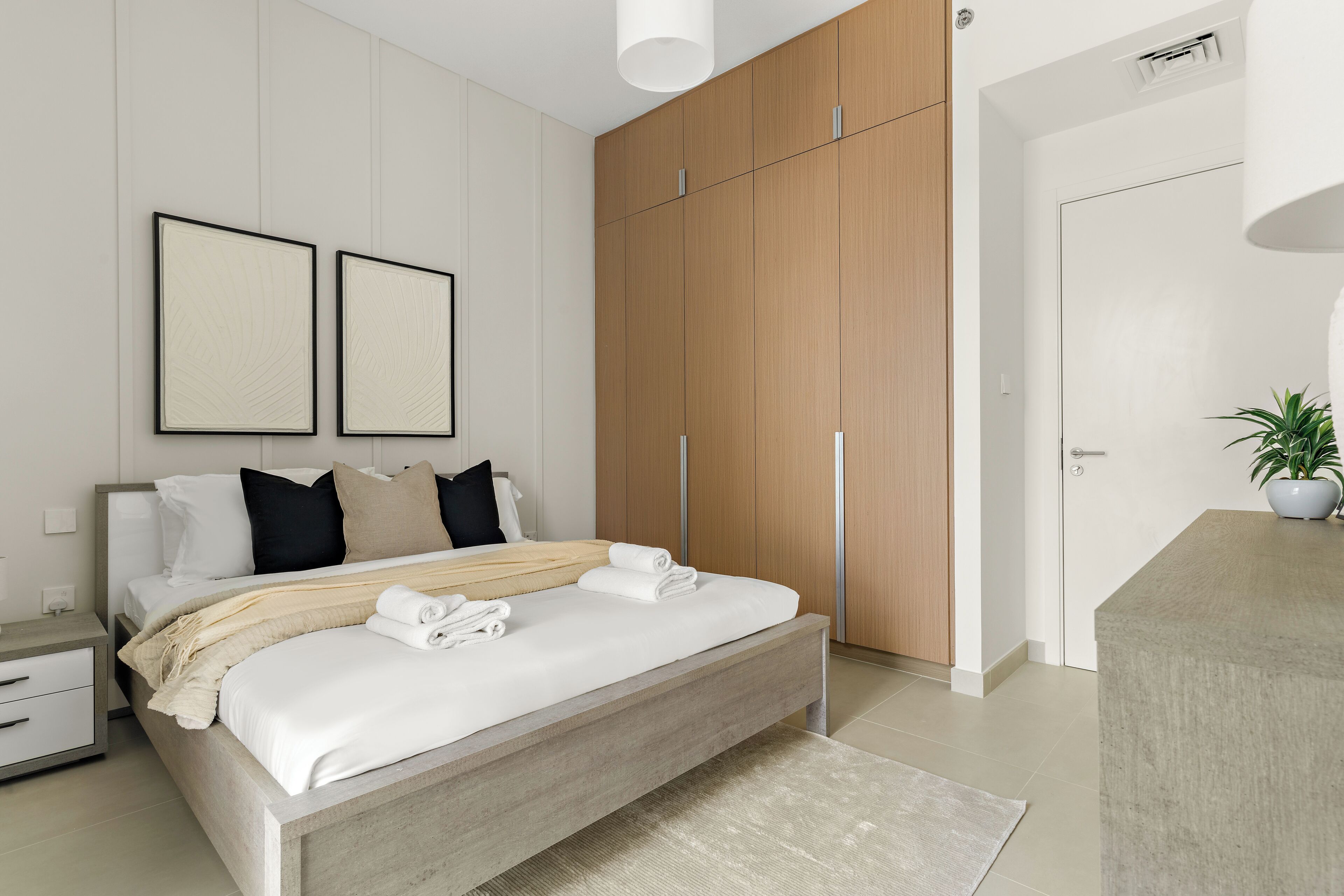 A modern bedroom with a bed, bedside tables, a wardrobe, and a potted plant.