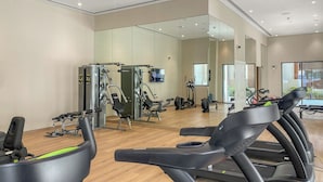 Une salle de sport équipée de tapis de course, d’appareils de musculation et d’un mur recouvert de miroirs.