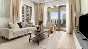 Un salon moderne comprenant un canapé, un fauteuil, une table basse et un téléviseur. Il y a un balcon avec vue sur les immeubles.