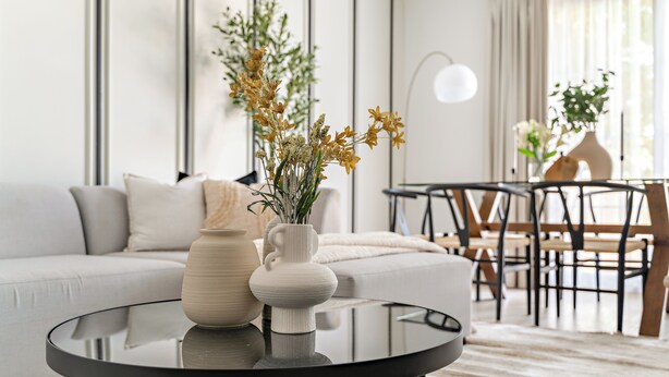 A modern living room with a round glass coffee table, a white sofa, and a dining area with wooden chairs and a table. - Silkhaus Springs 7 (Dubai)