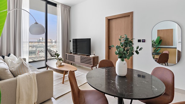 Een moderne woonkamer met een bank, eettafel en stoelen, een televisie en een groot raam met gordijnen.