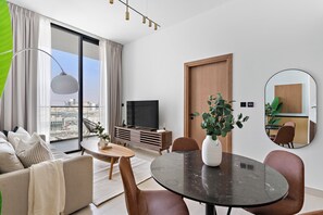 Un salon moderne comprenant un canapé, une table à manger et des chaises, un téléviseur et une grande fenêtre avec des rideaux.