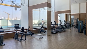 Een sportschool met trainingsapparatuur, grote ramen en uitzicht op bouwkranen.