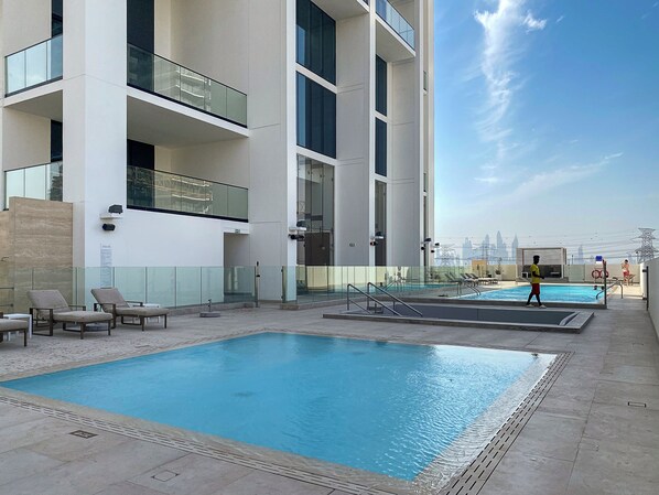 A rooftop pool area with a large pool, lounge chairs, and a city skyline view.