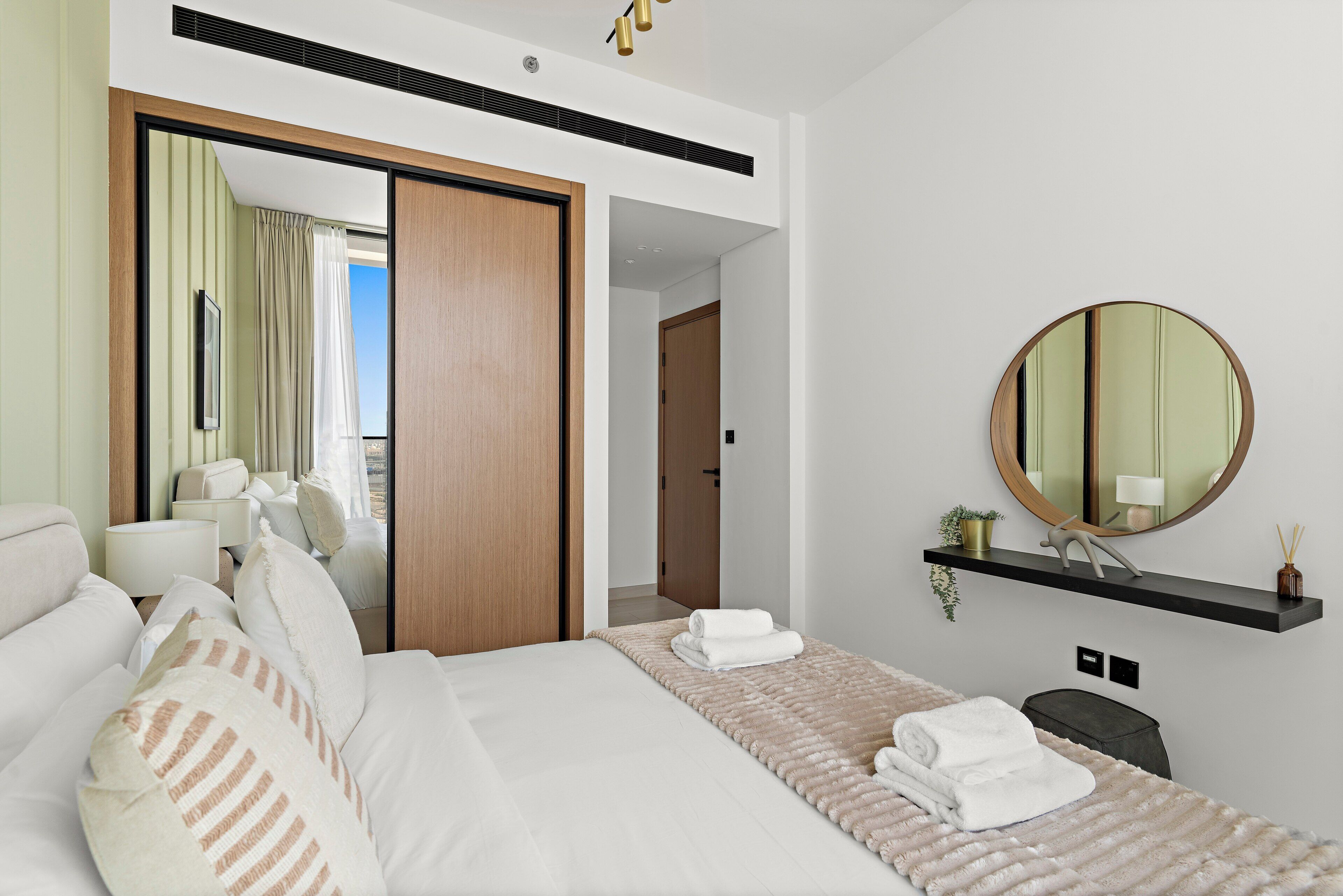A modern hotel room with a large bed, a bedside table, a mirror, and a view of the balcony.