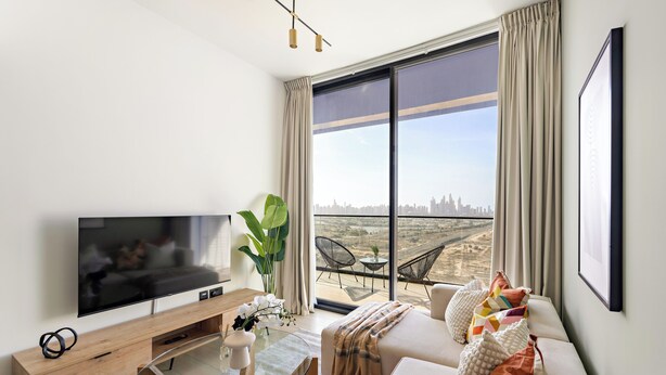 A modern living room with a large TV, a glass coffee table, a sofa with cushions, and a view of a cityscape through large windows. - Silkhaus Binghatti Corner (Dubai)