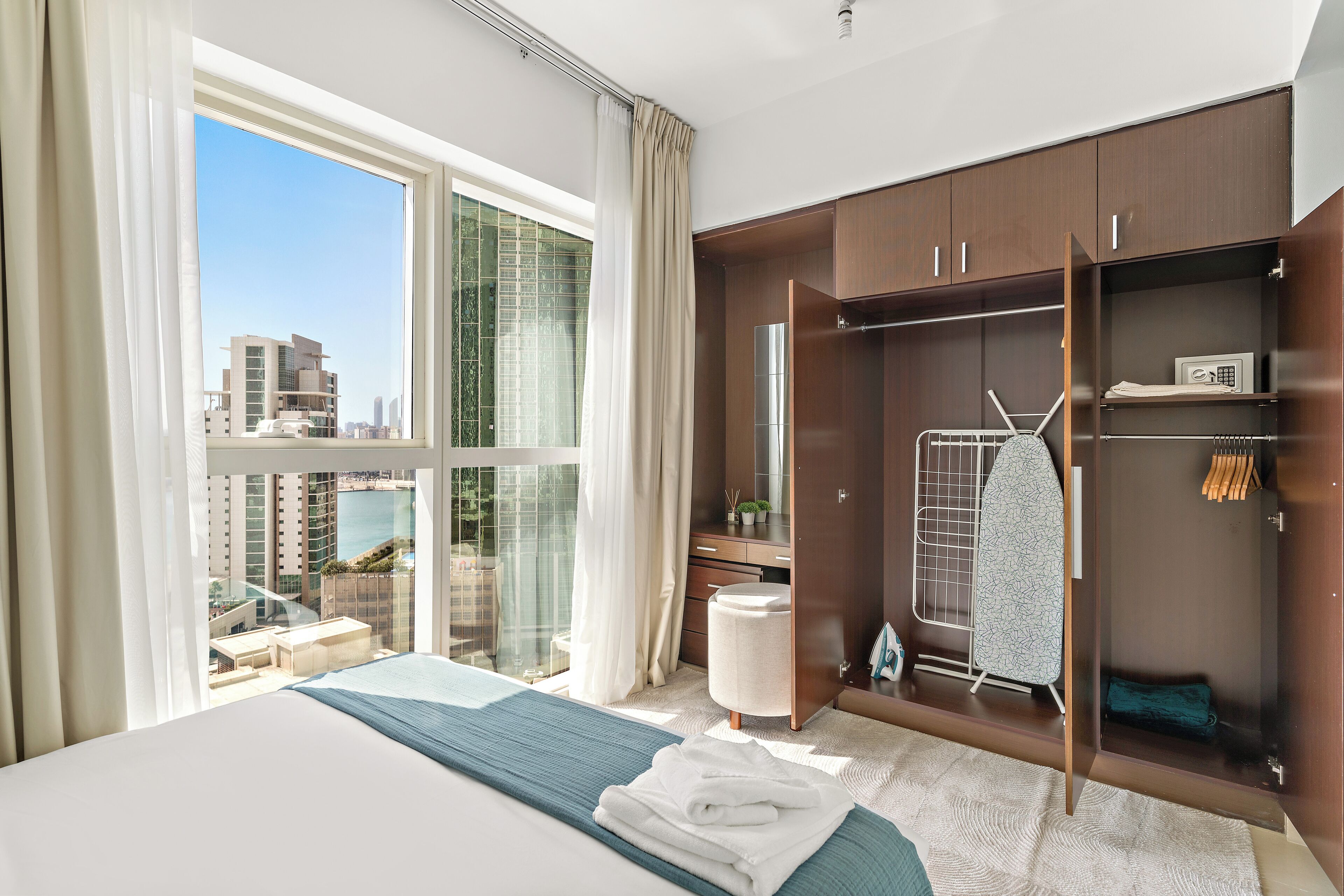 A hotel room with a large window, a bed, a wardrobe, and a small seating area.