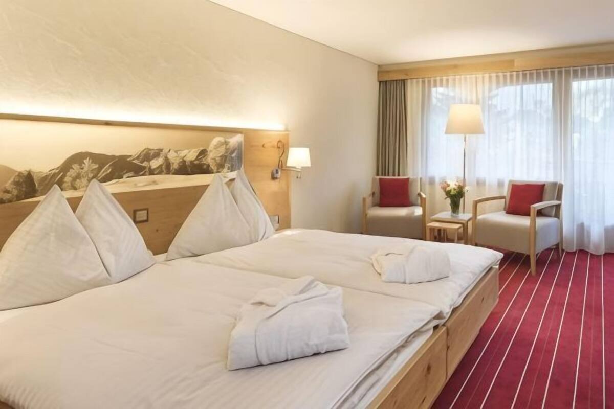 A hotel room with a large bed, two bedside tables, a desk, a chair, and a window with curtains.